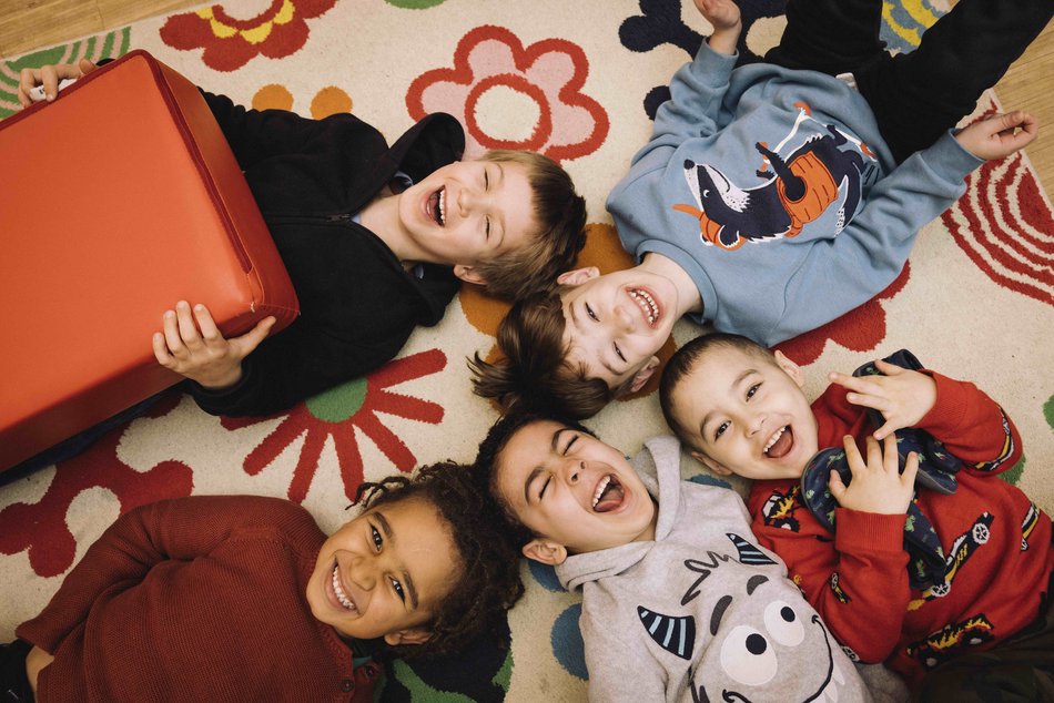 Kinder liegen im Kreis auf dem Boden und lachen in die Kamera