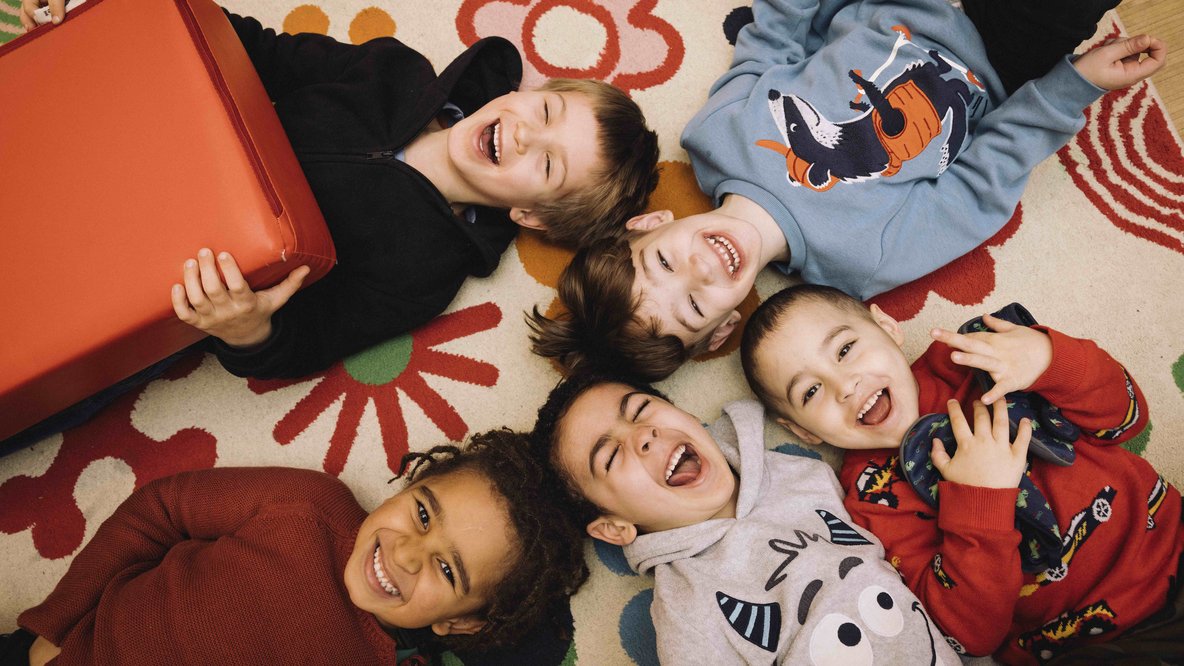 Kinder liegen im Kreis auf dem Boden und lachen in die Kamera