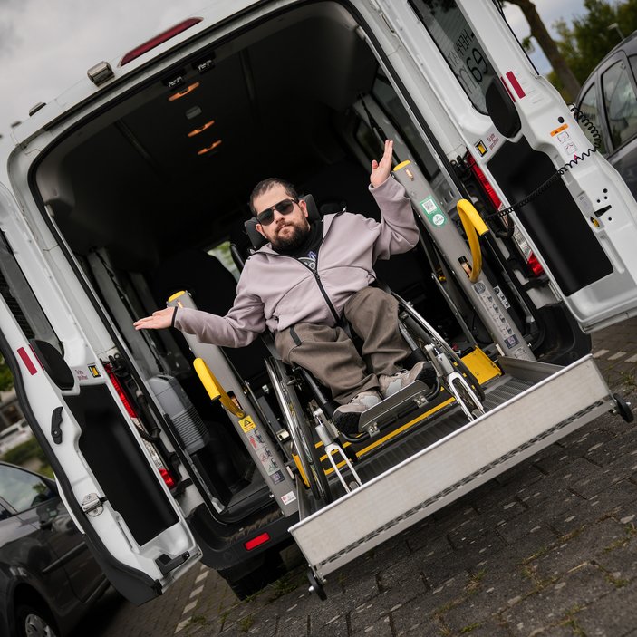 Leo sitzt im Rollstuhl und ist im Rückteil eines Busses des Fahrdienstes, der die Rollstuhlrampe ausgefahren hat
