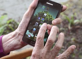 Hände einer älteren Person halten ein Smartphone in der Hand 