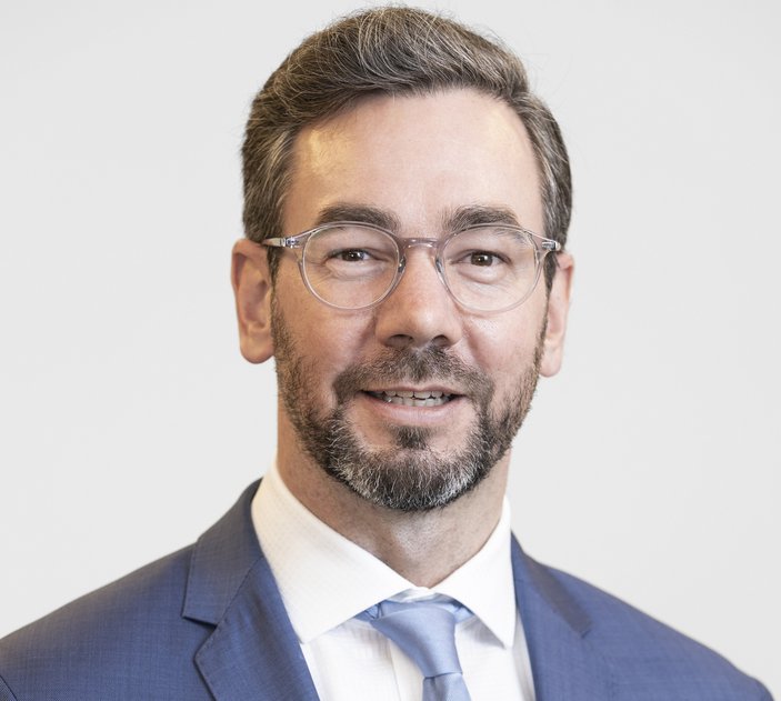 Ein Mann mit Brille und Bart schaut lächelnd nach vorne.