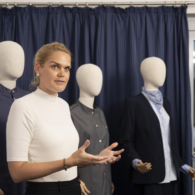 Eine Mitarbeiterin steht vor drei Modepuppen, die nachhaltige Kleidung tragen