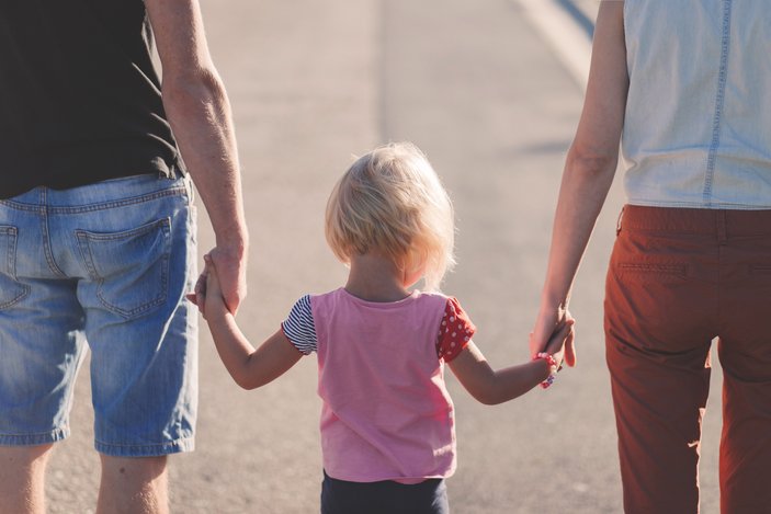 zwei erwachsene Menschen und ein Kind sind von hinten zu sehen, sie halten sich an den Händen