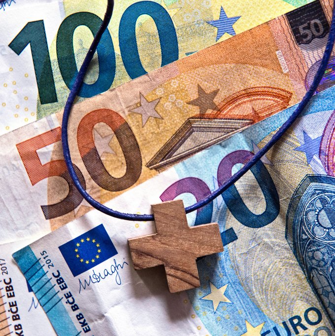 Eine Kette mit einem kleinen Holzkreuz liegt auf drei Euro-Banknoten
