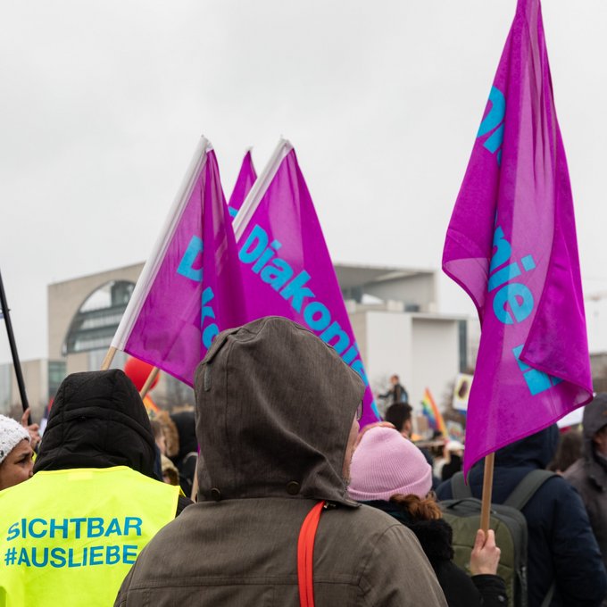 Menschen halten bei einer Demonstration in Berlin Diakonie-Fahnen