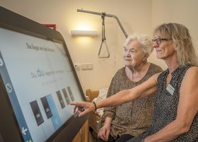 Eine Altenpflegerin zeigt einer Klientin eine digitale Tafel