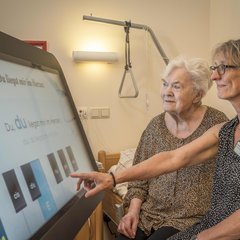 Eine Altenpflegerin zeigt einer Klientin eine digitale Tafel