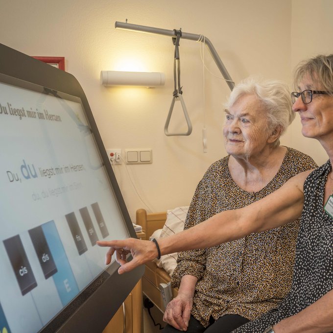 Eine Altenpflegerin zeigt einer Klientin eine digitale Tafel