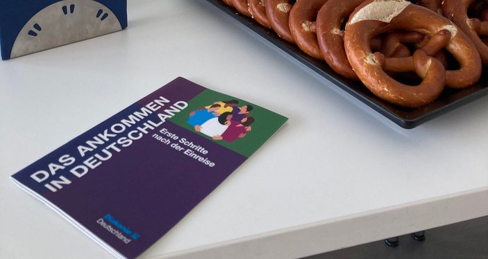 Eine Broschüre der Diakonie zum Ankommen in Deutschland liegt auf einem Tisch, daneben stehen Obst und Brezeln